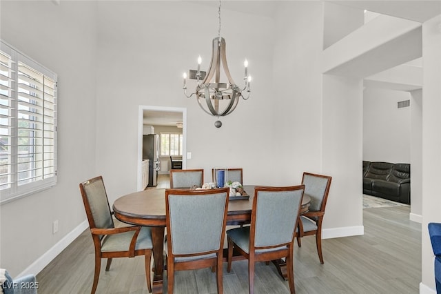dining area with a towering ceiling, visible vents, wood finished floors, baseboards, and an inviting chandelier