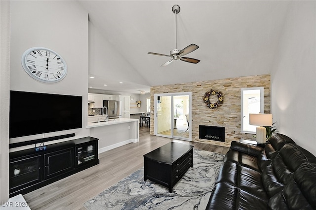 living area featuring light wood finished floors, high vaulted ceiling, a large fireplace, a ceiling fan, and recessed lighting