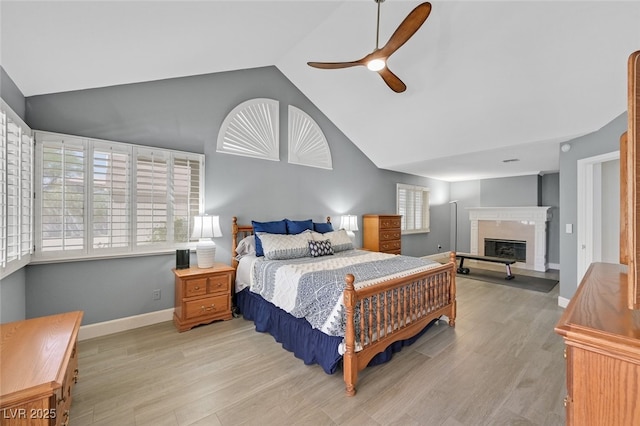 bedroom with a ceiling fan, wood finished floors, high vaulted ceiling, baseboards, and a glass covered fireplace