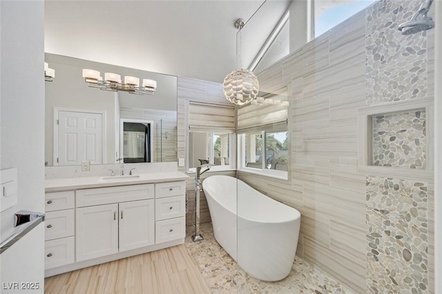bathroom featuring vanity, tile walls, an inviting chandelier, and a freestanding bath