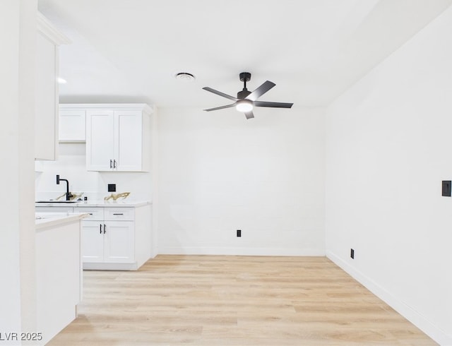 kitchen featuring a sink, ceiling fan, light wood-type flooring, and white cabinetry