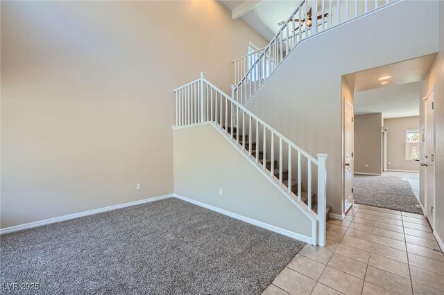 staircase with carpet flooring, a high ceiling, beam ceiling, tile patterned floors, and baseboards