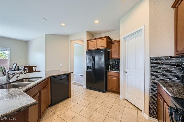 kitchen with a sink, dark stone counters, light tile patterned floors, backsplash, and black appliances