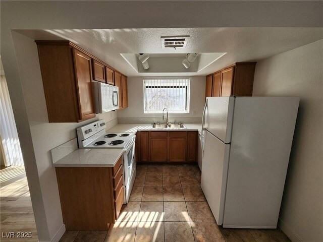 kitchen with a sink, a raised ceiling, white appliances, light countertops, and visible vents