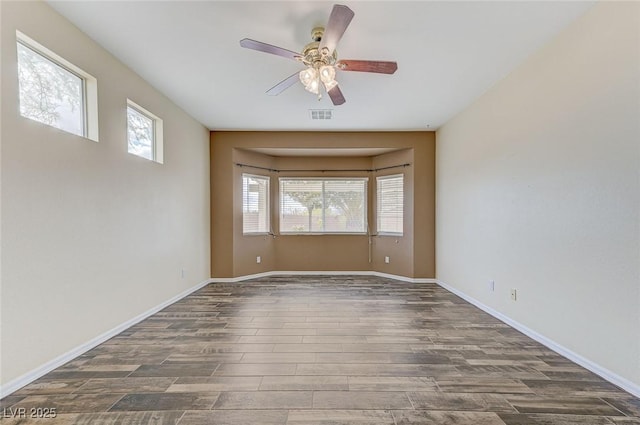 spare room featuring dark wood-style flooring, ceiling fan, visible vents, and baseboards