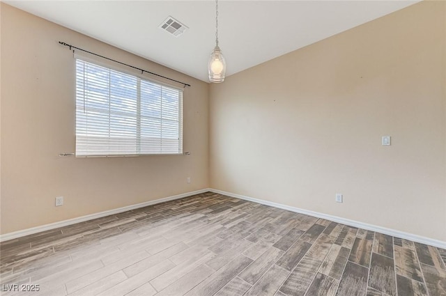 unfurnished room featuring baseboards, visible vents, and wood finished floors