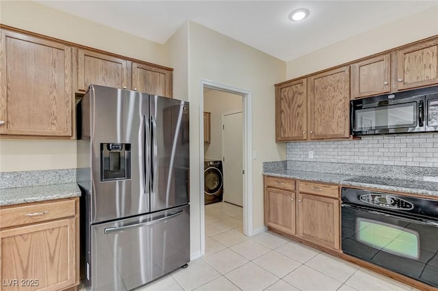 kitchen with decorative backsplash, washer / clothes dryer, light stone countertops, light tile patterned floors, and black appliances