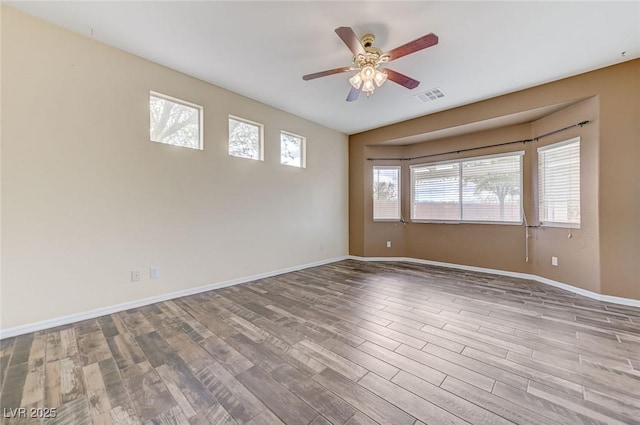 empty room with ceiling fan, visible vents, plenty of natural light, and wood finished floors