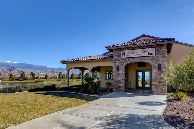 exterior space featuring stone siding, stucco siding, french doors, a tiled roof, and a lawn
