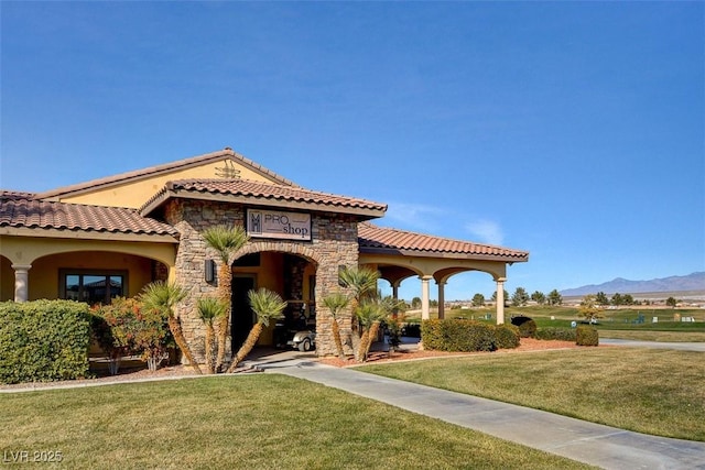 mediterranean / spanish-style home featuring a front lawn, stone siding, stucco siding, a mountain view, and a tiled roof