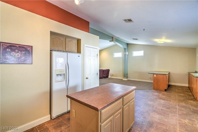kitchen featuring arched walkways, white fridge with ice dispenser, baseboards, a kitchen island, and visible vents