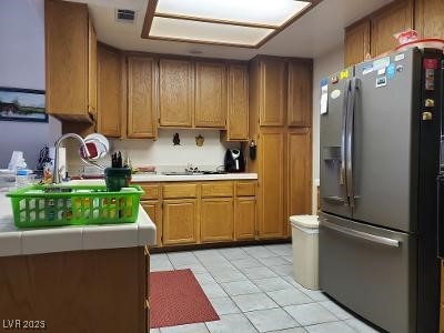 kitchen with stainless steel fridge, a sink, light tile patterned floors, and brown cabinets
