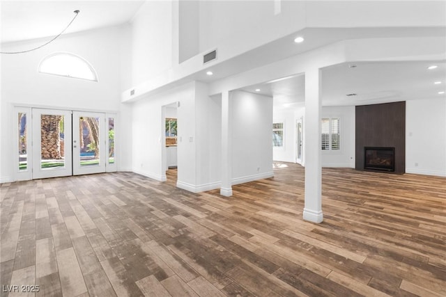 unfurnished living room featuring visible vents, hardwood / wood-style flooring, baseboards, a high ceiling, and recessed lighting