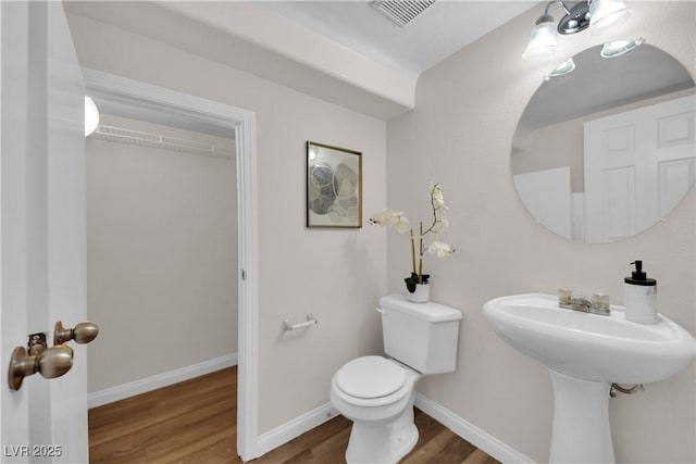 half bath featuring visible vents, baseboards, wood finished floors, and toilet