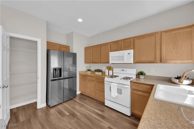 kitchen featuring white appliances, light wood-type flooring, recessed lighting, light countertops, and a sink
