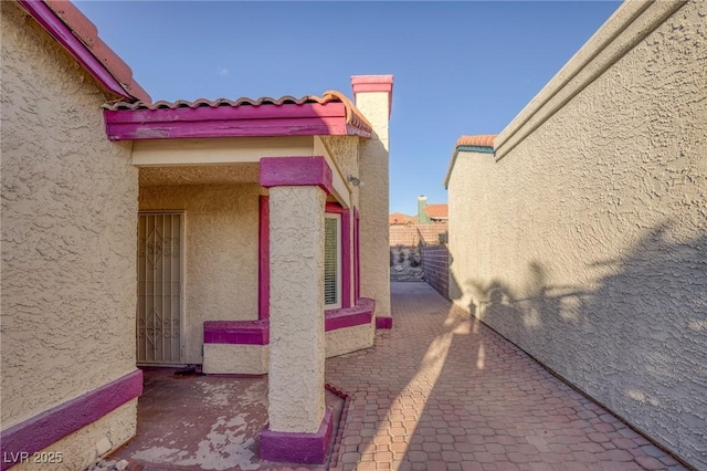view of side of home featuring a patio, stucco siding, a tile roof, and fence