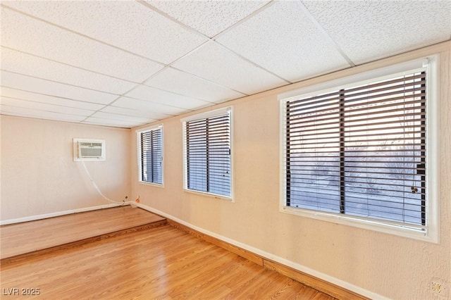 spare room featuring baseboards, a wall mounted air conditioner, wood finished floors, and a paneled ceiling