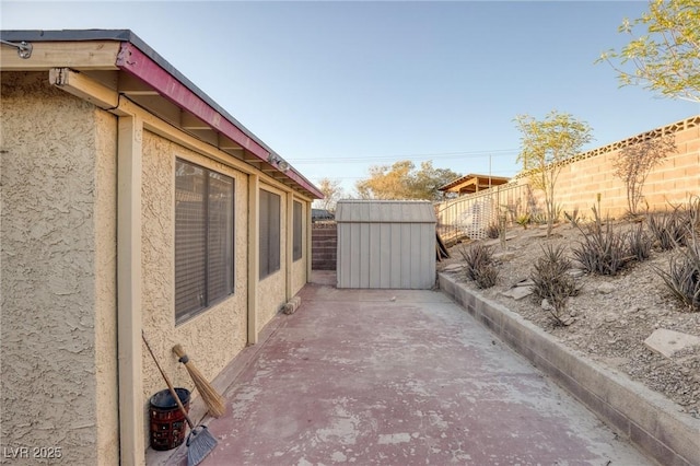 view of property exterior with an outbuilding, a fenced backyard, a storage unit, a patio, and stucco siding