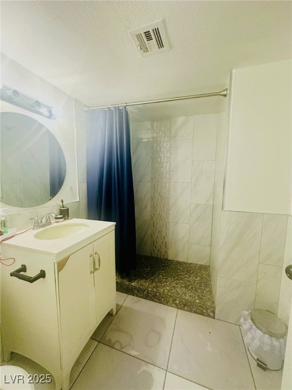 full bath with vanity, a tile shower, a textured ceiling, and visible vents