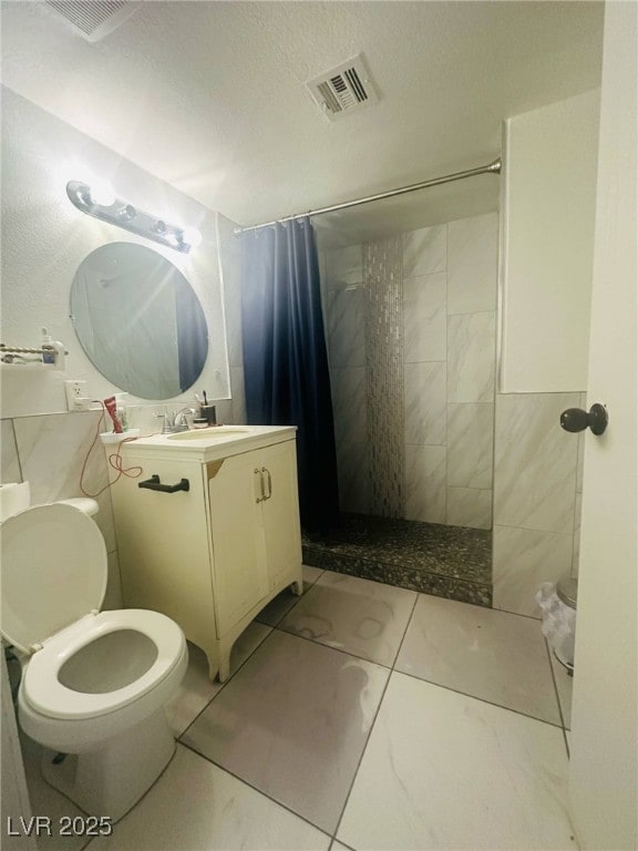 bathroom with toilet, visible vents, a tile shower, and vanity