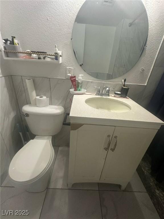 bathroom featuring vanity, a textured wall, tile patterned floors, and toilet