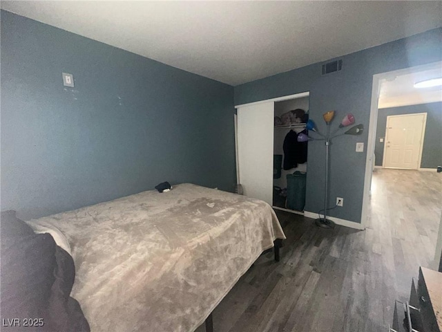 bedroom with baseboards, visible vents, wood finished floors, and a closet