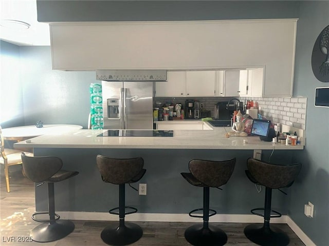kitchen with a peninsula, black electric stovetop, a kitchen bar, light countertops, and stainless steel fridge with ice dispenser