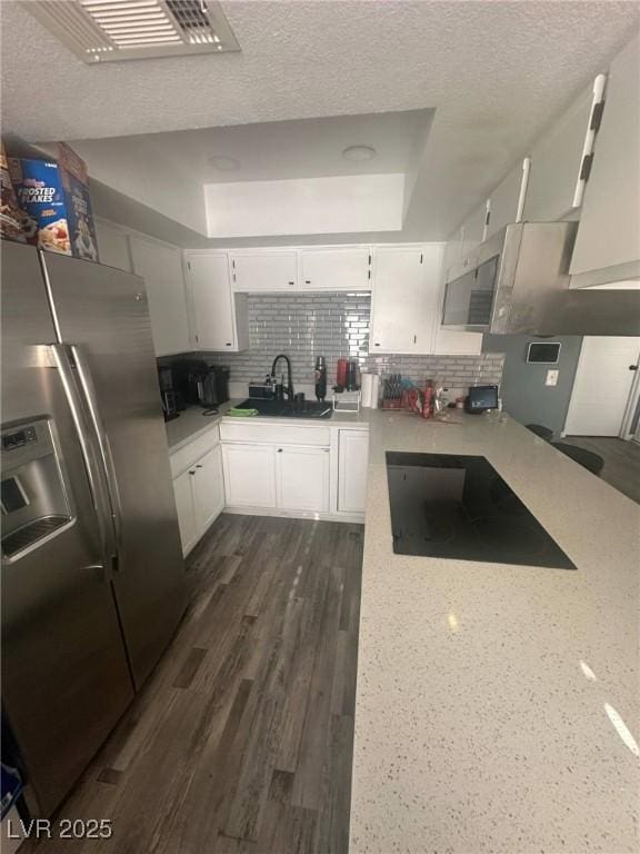 kitchen featuring black electric stovetop, stainless steel fridge, a sink, a textured ceiling, and backsplash