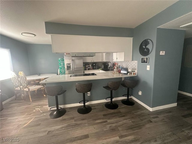 kitchen with black electric stovetop, a sink, a peninsula, white cabinetry, and tasteful backsplash