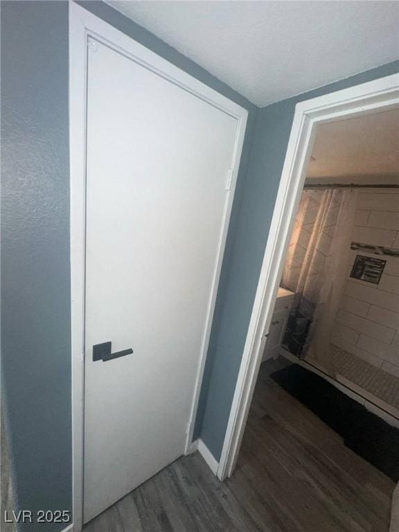 full bath with baseboards, wood finished floors, and tiled shower