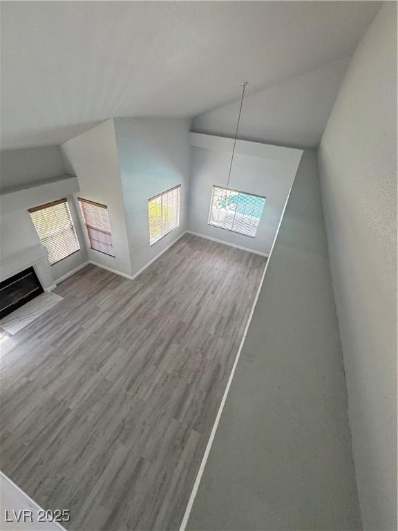 additional living space featuring baseboards, a fireplace, wood finished floors, and lofted ceiling
