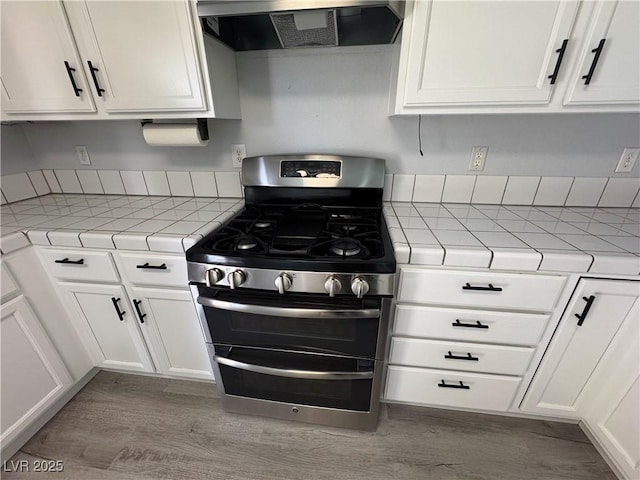 kitchen featuring exhaust hood, range with two ovens, tile counters, and white cabinetry