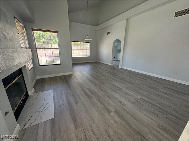 unfurnished living room featuring visible vents, arched walkways, wood finished floors, baseboards, and a glass covered fireplace