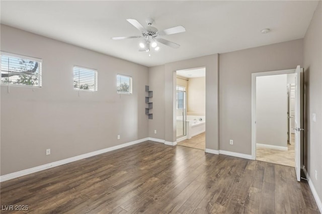 unfurnished bedroom with baseboards, ensuite bath, wood finished floors, and ceiling fan