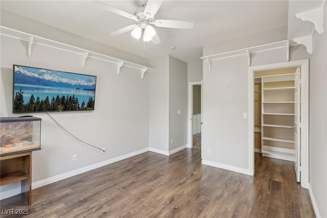 unfurnished bedroom featuring baseboards, a ceiling fan, a walk in closet, and wood finished floors