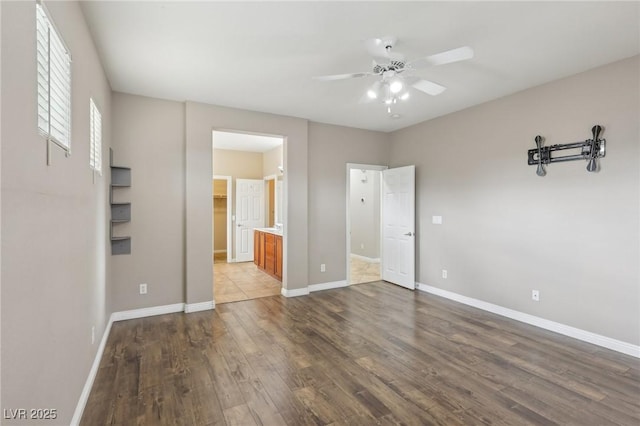 unfurnished bedroom featuring baseboards, a ceiling fan, ensuite bathroom, and wood finished floors