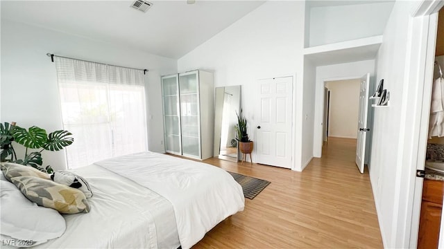 bedroom with visible vents, light wood-style flooring, baseboards, and high vaulted ceiling