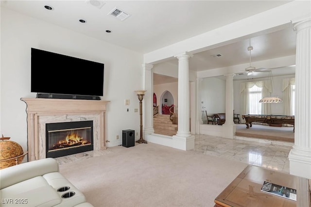 living area featuring a premium fireplace, decorative columns, and visible vents