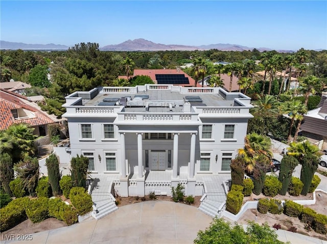 greek revival inspired property featuring a balcony, stucco siding, stairs, roof mounted solar panels, and a mountain view