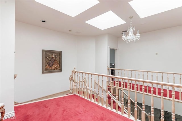 hall with an inviting chandelier, carpet flooring, a skylight, and an upstairs landing