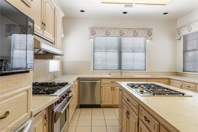 kitchen featuring appliances with stainless steel finishes, a sink, light countertops, light brown cabinets, and under cabinet range hood