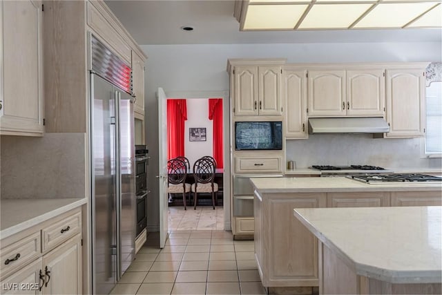 kitchen with stainless steel appliances, decorative backsplash, light tile patterned floors, under cabinet range hood, and a warming drawer