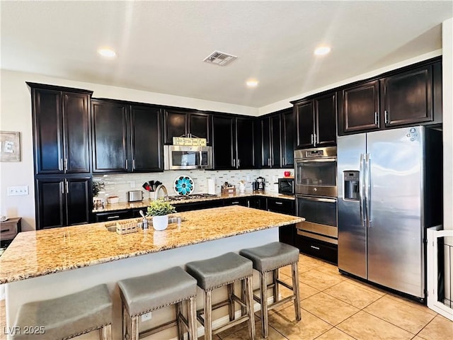 5634 Bishop Flowers St, Las Vegas, NV 89130 - kitchen with stainless steel appliances, a breakfast bar area, light stone countertops, backsplash, and light tile patterned flooring