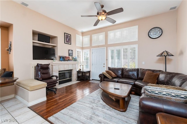 living area with visible vents, wood finished floors, baseboards, a tile fireplace, and a ceiling fan