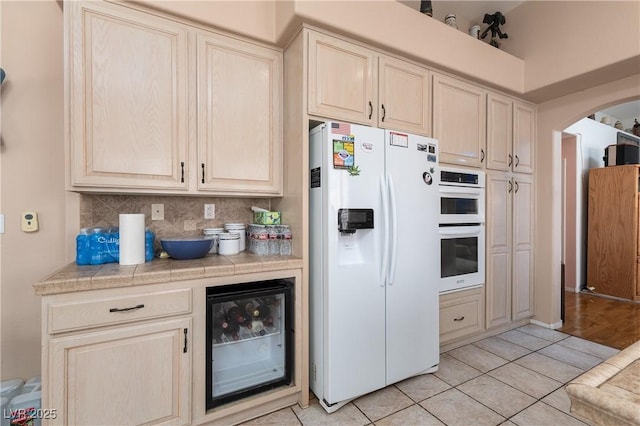 kitchen with wine cooler, white appliances, tasteful backsplash, arched walkways, and light tile patterned floors