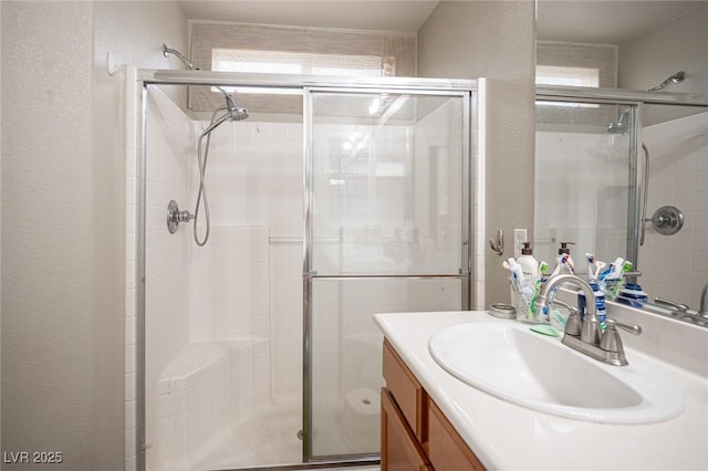 full bath with a textured wall, a shower stall, and vanity