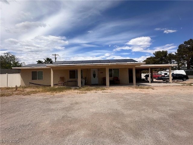 view of front of house with stucco siding, fence, covered porch, and solar panels