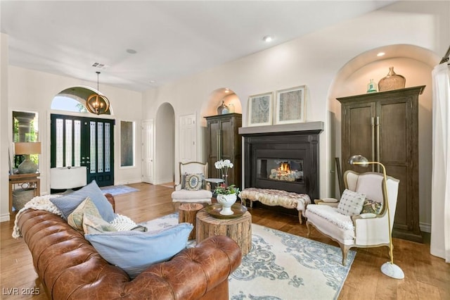living area with arched walkways, a glass covered fireplace, baseboards, wood finished floors, and visible vents