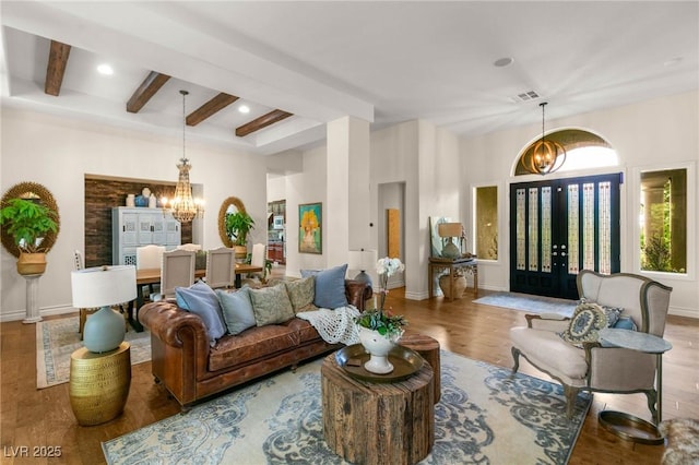living room with an inviting chandelier, visible vents, beam ceiling, wood finished floors, and baseboards