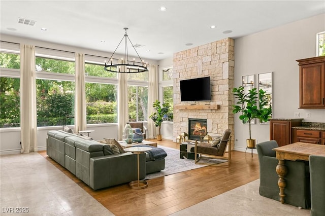 living room with a healthy amount of sunlight, a notable chandelier, a stone fireplace, and visible vents